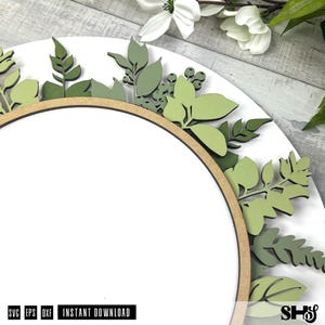 May include: A circular wooden sign featuring a white center and a border decorated with layered, laser-cut wooden leaves in various shades of sage and olive green. The text SVG, EPS, DXF, INSTANT DOWNLOAD is printed at the bottom left corner.