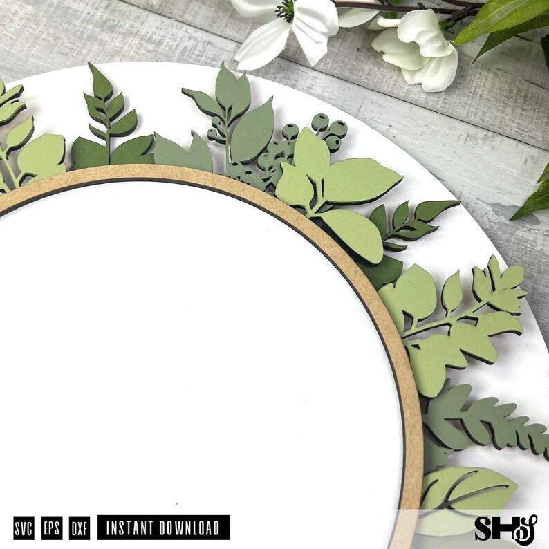 May include: A circular wooden sign featuring a white center and a border decorated with layered, laser-cut wooden leaves in various shades of sage and olive green. The text SVG, EPS, DXF, INSTANT DOWNLOAD is printed at the bottom left corner.