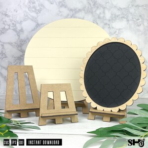 K&ouml;nnte beinhalten: Ein gro&szlig;es rundes Schild aus hellem Holz mit horizontalen Linien, ein kleineres rundes schwarzes Schild mit gewelltem Rand und Vierpassmuster sowie zwei Staffeleien aus hellem Holz zum Aufstellen der runden Schilder auf einer Fl&auml;che.