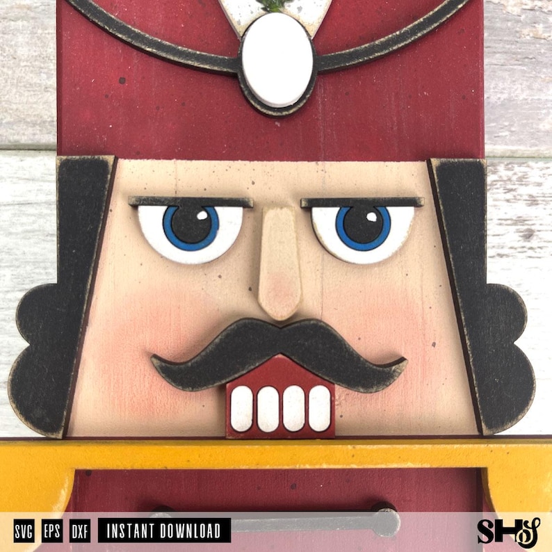 May include: A wooden nutcracker face cutout featuring a deep red hat with a white oval emblem, black hair, blue eyes, a prominent nose, a black moustache, and white teeth. The design includes a yellow collar and the text SVG EPS DXF INSTANT DOWNLOAD.