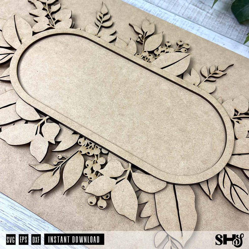 May include: A wooden cutout of a floral wreath with an oval-shaped blank space in the center. The wreath is made of leaves and berries.