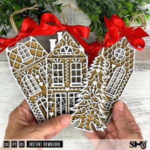 Puede incluir: Tres adornos navide&ntilde;os de madera cortados con l&aacute;ser con forma de casas de jengibre y un &aacute;rbol de Navidad. Cada adorno tiene un dise&ntilde;o superpuesto blanco, un respaldo marr&oacute;n y una cinta roja para colgar. Los adornos son sostenidos por manos.
