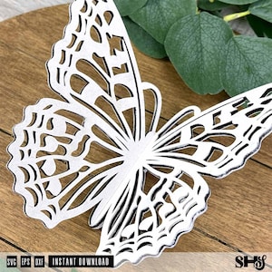May include: A white butterfly cutout with intricate, lace-like filigree patterns throughout its wings. The butterfly features a detailed, symmetrical design with scalloped edges and open spaces, showcasing a clean, high-contrast aesthetic.