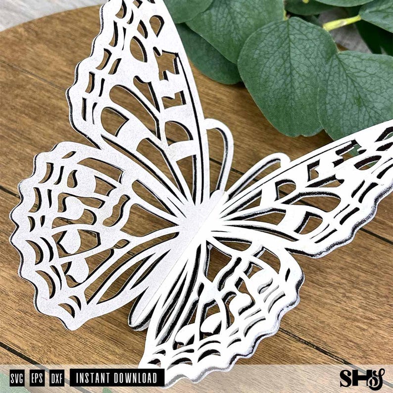 May include: A white butterfly cutout with intricate, lace-like filigree patterns throughout its wings. The butterfly features a detailed, symmetrical design with scalloped edges and open spaces, showcasing a clean, high-contrast aesthetic.