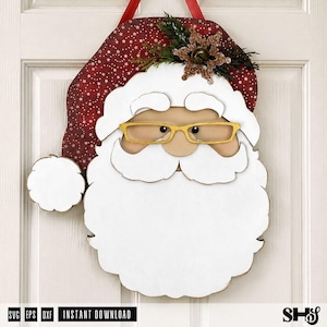 K&ouml;nnte beinhalten: Ein Weihnachtsmann-T&uuml;rh&auml;nger mit einer roten M&uuml;tze mit wei&szlig;em Sternenmuster, einem gro&szlig;en wei&szlig;en Bart und einer goldfarbenen Brille. Die M&uuml;tze ist mit einem glitzernden braunen Schneeflocken-Ornament und gr&uuml;nen Tannennadeln verziert.