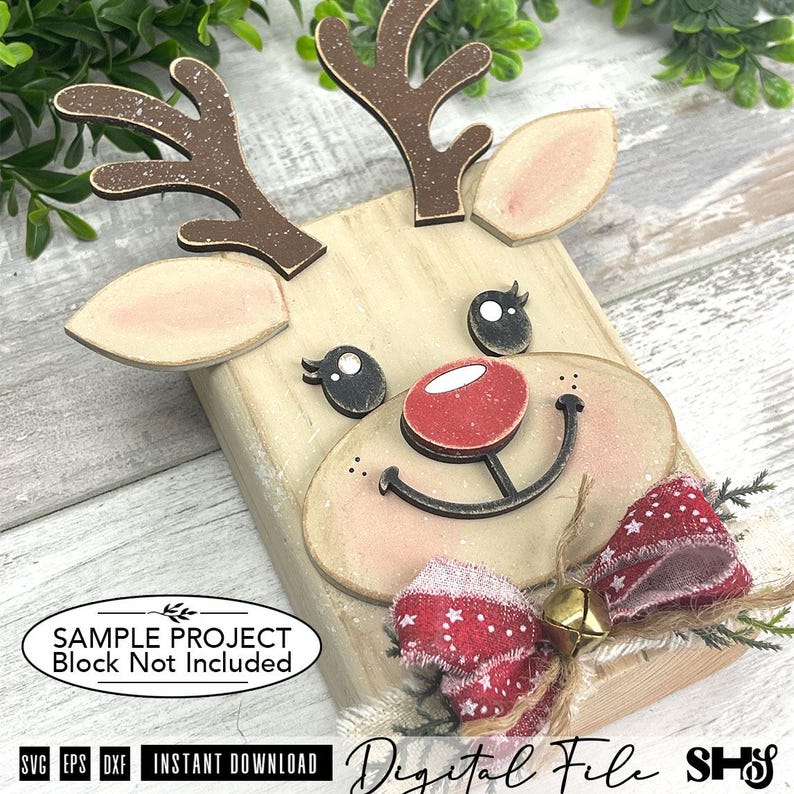 Pu&ograve; includere: Un progetto artigianale in legno a forma di renna con corna marroni a macchie bianche, naso rosso, occhi neri e un fiocco in tessuto rosso a motivi con un campanellino dorato. Il testo riporta SAMPLE PROJECT Block Not Included e Digital File.