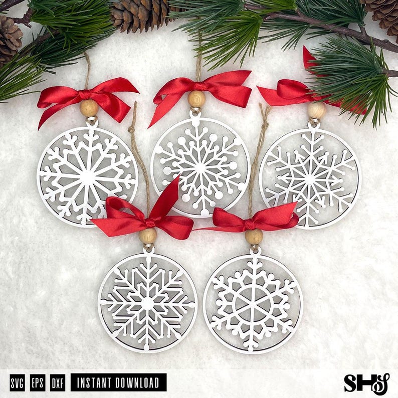 May include: Five circular white snowflake ornaments made of wood, each featuring a unique intricate cutout pattern. Every ornament is topped with a natural wooden bead and a vibrant red satin ribbon bow, suspended by a thin twine string.