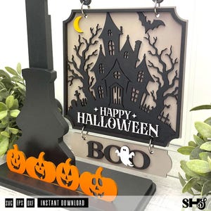 May include: A layered wooden sign featuring a black haunted house silhouette, a yellow crescent moon, and a bat against a beige background. The text reads HAPPY HALLOWEEN and BOO with a white ghost. Four orange jack-o'-lanterns sit at the base.