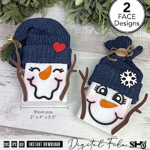 May include: Two snowman figures made of white blocks with navy blue knit hats, orange carrot noses, and brown branch-like arms. One features a red heart, the other a white snowflake. Text indicates 2 face designs and a 2 inch by 4 inch by 5.5 inch block size.
