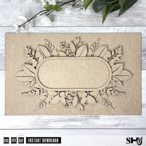 May include: A wooden cutout of a floral wreath with a blank oval in the center. The wreath is made of leaves and flowers, and the oval is perfect for adding a personalized message.