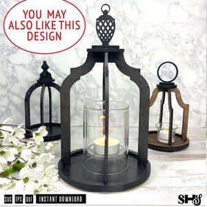 May include: Three black wooden lantern frames with arched supports and circular bases. The central lantern holds a clear glass cylinder with a lit tea light candle. Each frame features a decorative top finial and a ring handle for hanging.