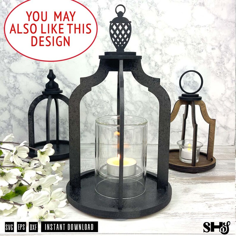 May include: Three black wooden lantern frames with arched supports and circular bases. The central lantern holds a clear glass cylinder with a lit tea light candle. Each frame features a decorative top finial and a ring handle for hanging.