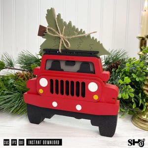 Puede incluir: Un cami&oacute;n de juguete de madera rojo con portaequipajes y neum&aacute;ticos negros. Un &aacute;rbol de Navidad de madera verde est&aacute; atado al techo con cuerda marr&oacute;n. El cami&oacute;n tiene una parrilla frontal, faros blancos y luces de giro amarillas. El texto inferior dice SVG EPS DXF INSTANT DOWNLOAD.