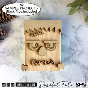 May include: A light-colored wooden block decorated with laser-cut wooden pieces forming a face. The design includes a jagged hairline, a stitched forehead scar, two eyes, a triangular nose, a stitched mouth, and two small rectangular side bolts.