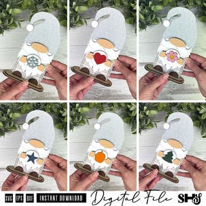 May include: A set of six layered wooden gnome ornaments featuring interchangeable centre icons including a snowflake, red heart, pink flower, blue star, orange pumpkin, and green tree. Each gnome wears a light blue hat with white polka dots.