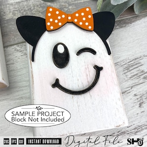 May include: A white wooden block featuring a ghost face with black eyes and a curved mouth. The ghost has black ears and an orange bow with white polka dots attached to the top. The text on the image reads: SAMPLE PROJECT Block Not Included.
