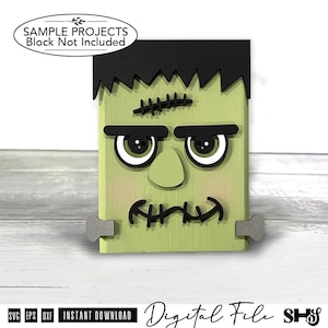 May include: A light green rectangular wooden block decoration featuring a black hair piece, thick black eyebrows, large white eyes with black pupils, a nose, and a stitched mouth. Two grey bolts are attached to the sides of the block.