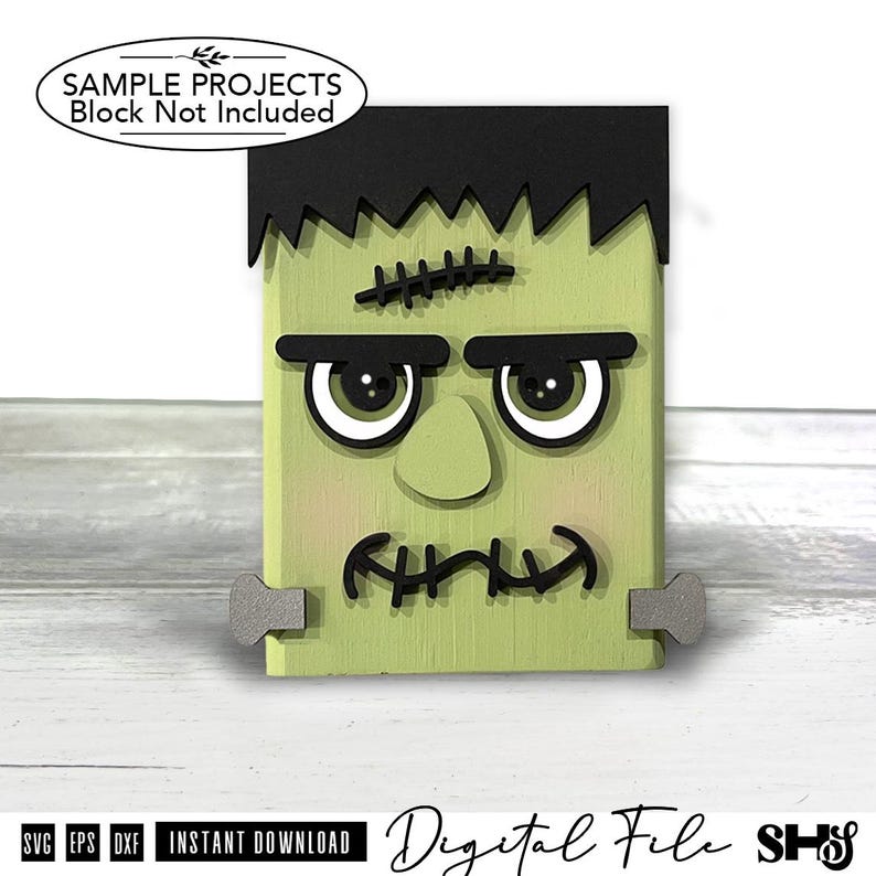May include: A light green rectangular wooden block decoration featuring a black hair piece, thick black eyebrows, large white eyes with black pupils, a nose, and a stitched mouth. Two grey bolts are attached to the sides of the block.