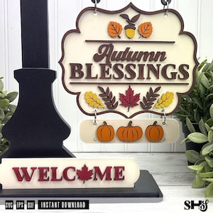 Puede incluir: Un letrero de madera en capas con el texto Autumn Blessings en marrón oscuro, decorado con hojas naranjas y amarillas y una bellota. Debajo, una pieza rectangular muestra tres calabazas naranjas. Una base separada muestra el texto WELCOME.