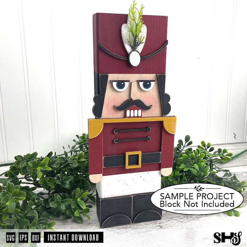 May include: A wooden nutcracker figure featuring a tall maroon hat with a white plume, a black moustache, blue eyes, and a red jacket with gold shoulder accents. The figure has a black belt with a gold buckle, white trousers, and black boots.