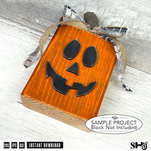 May include: A rectangular wooden block painted orange with a black jack-o'-lantern face featuring two oval eyes, a triangular nose, and a jagged mouth. The top is decorated with a brown burlap ribbon and a black and white plaid fabric ribbon.