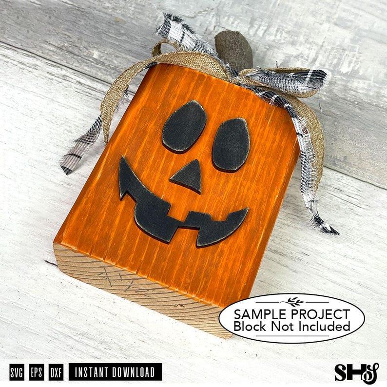 May include: A rectangular wooden block painted orange with a black jack-o'-lantern face featuring two oval eyes, a triangular nose, and a jagged mouth. The top is decorated with a brown burlap ribbon and a black and white plaid fabric ribbon.