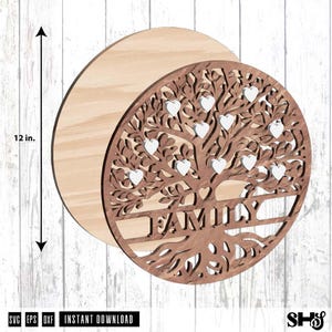 May include: A circular wooden wall art piece featuring a laser-cut tree design with the word FAMILY integrated into the trunk. The design includes multiple small white heart-shaped cutouts nestled within the branches. A 12-inch measurement is indicated.