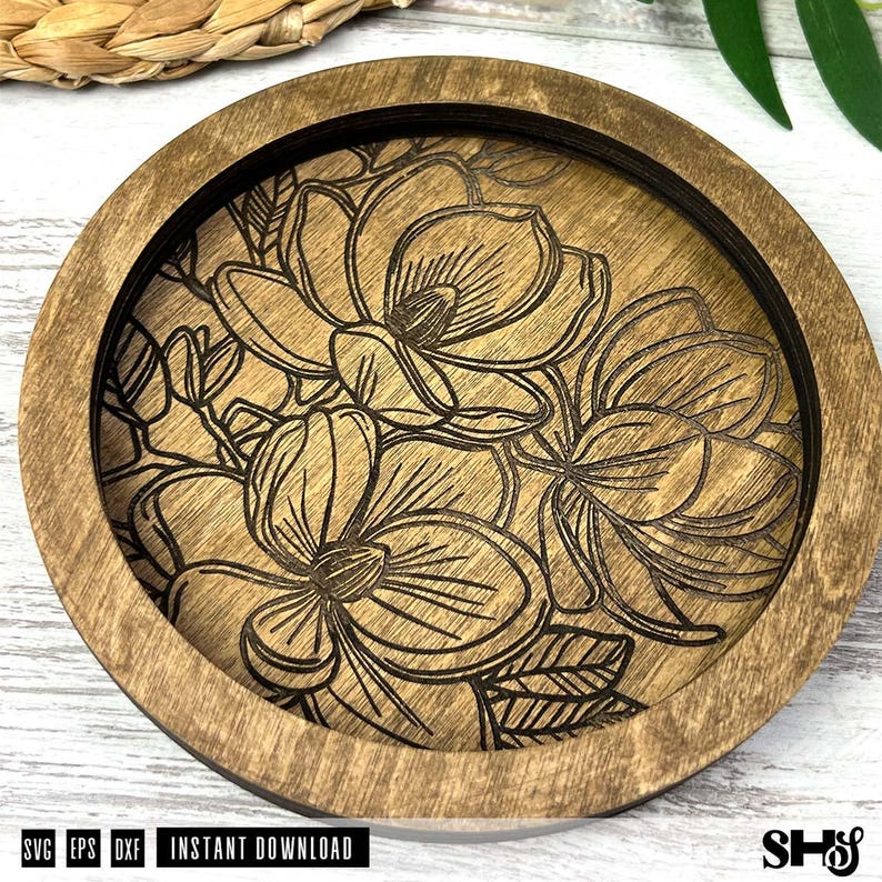 May include: A circular wooden coaster featuring a dark brown stained frame and a lighter brown center panel. The center panel is laser-engraved with a detailed floral pattern of multiple blooming flowers and leaves with dark, thin lines.
