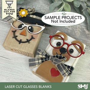 May include: Two wooden laser-cut blanks, one resembling a scarecrow and the other a bear, each with glasses. The scarecrow has white glasses, a black hat, and a yellow flower. The bear has red glasses and a plaid bow. The text "LASER CUT GLASSES BLANKS" is at the bottom.