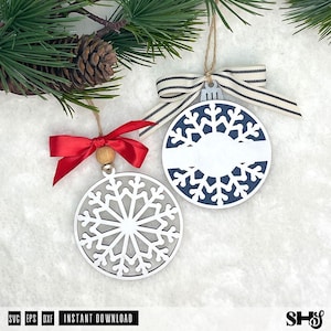 May include: Two circular snowflake ornaments. One is white with a grey background and a red satin ribbon bow. The other is white with a dark blue background, a horizontal white centre bar, and a beige and black striped ribbon bow.