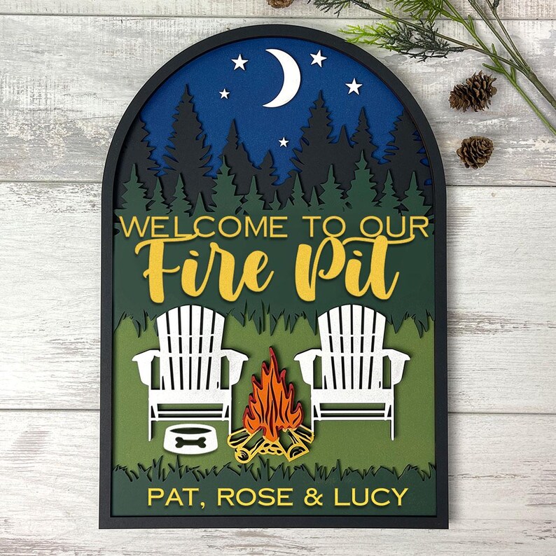 May include: An arched, layered wooden wall sign featuring a night scene with a crescent moon, stars, and a forest silhouette. The text reads "WELCOME TO OUR Fire Pit" and "PAT, ROSE & LUCY" above two white Adirondack chairs, a campfire, and a dog bowl.
