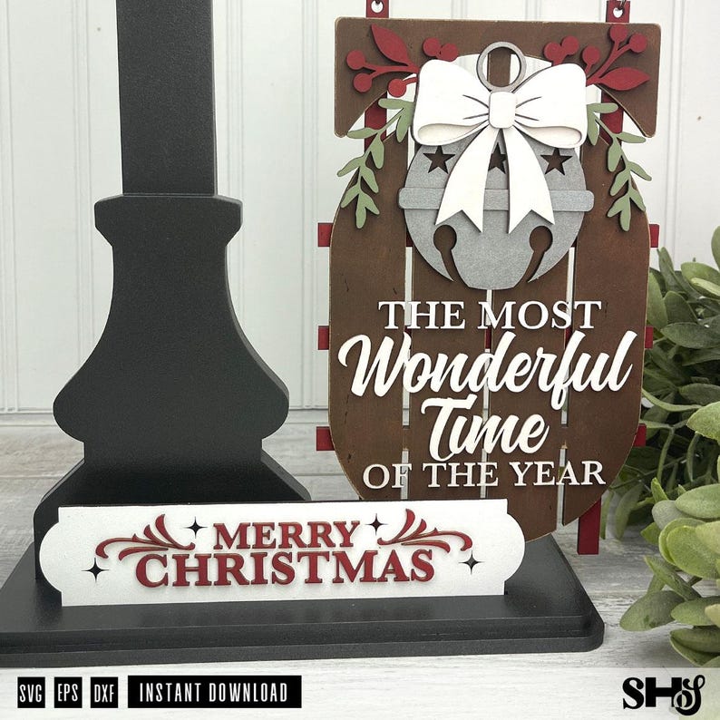 May include: A brown wooden sled-shaped sign featuring a grey jingle bell with a white bow, green leaves, and red berries. The text reads THE MOST WONDERFUL TIME OF THE YEAR. A separate white rectangular sign below reads MERRY CHRISTMAS in red.
