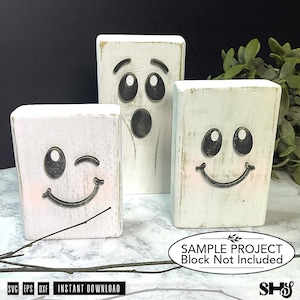 May include: Three rectangular white wooden blocks featuring black ghost faces. One block shows a winking face with a smile, another a surprised face with an open mouth, and the third a smiling face. Text on the image reads: SAMPLE PROJECT Block Not Included.