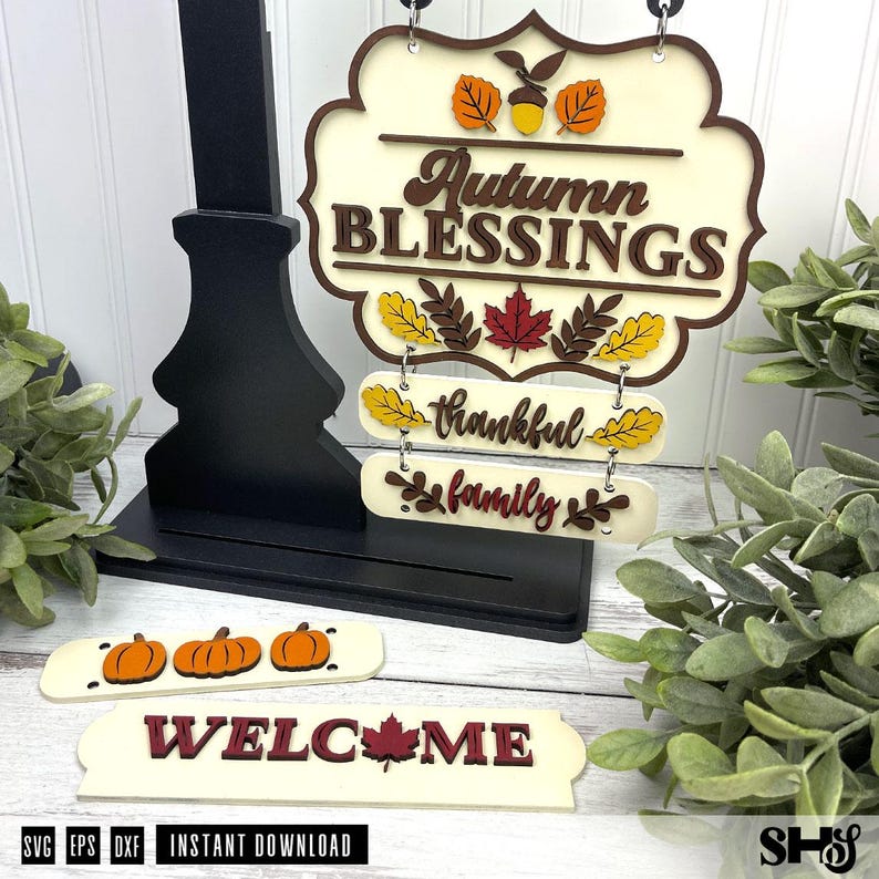Op de afbeelding: Een gelaagde houten bordenset met een cr&egrave;mekleurige plaat met de tekst Autumn BLESSINGS, versierd met een eikel en bladeren. Inclusief verwisselbare hangende latten met de woorden thankful en family, plus extra latten met pompoenen en WELCOME.