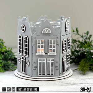 May include: A gray wooden candle holder shaped like a cluster of houses with white window frames and door outlines. The structure features multiple levels, arched and rectangular windows, and a circular opening at the top for a candle container.