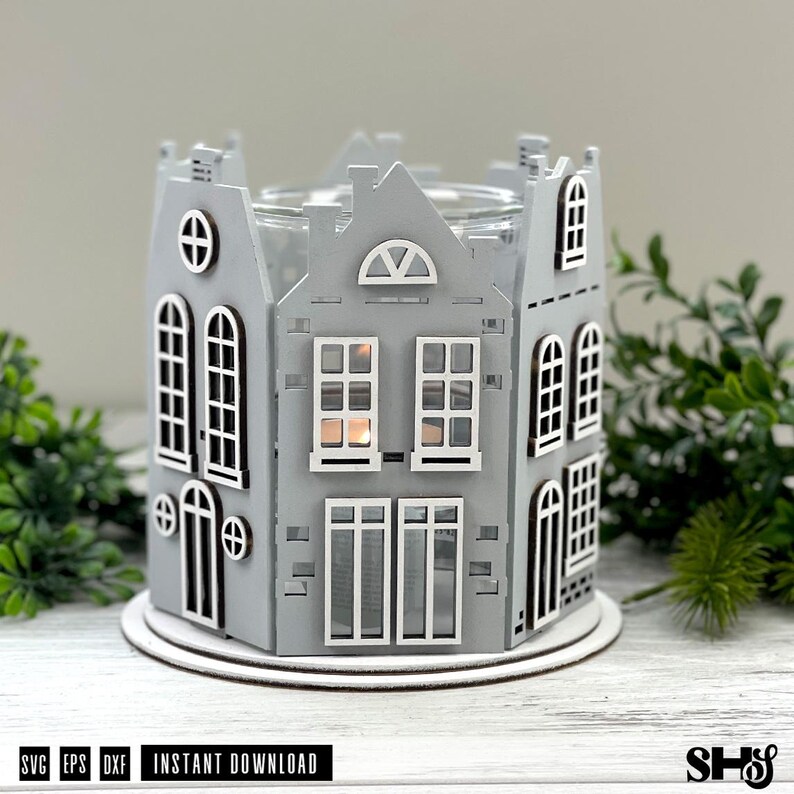 May include: A gray wooden candle holder shaped like a cluster of houses with white window frames and door outlines. The structure features multiple levels, arched and rectangular windows, and a circular opening at the top for a candle container.