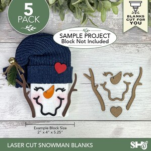 May include: A set of five laser-cut wooden snowman blanks including branch arms, a carrot nose, a mouth, and a heart. One assembled snowman features a navy blue knit hat, a red heart accent, and a painted face. Text includes 5 PACK, BLANKS CUT FOR YOU, SAMPLE PROJECT Block Not Included, and Example Block Size 2" x 4" x 5.25".