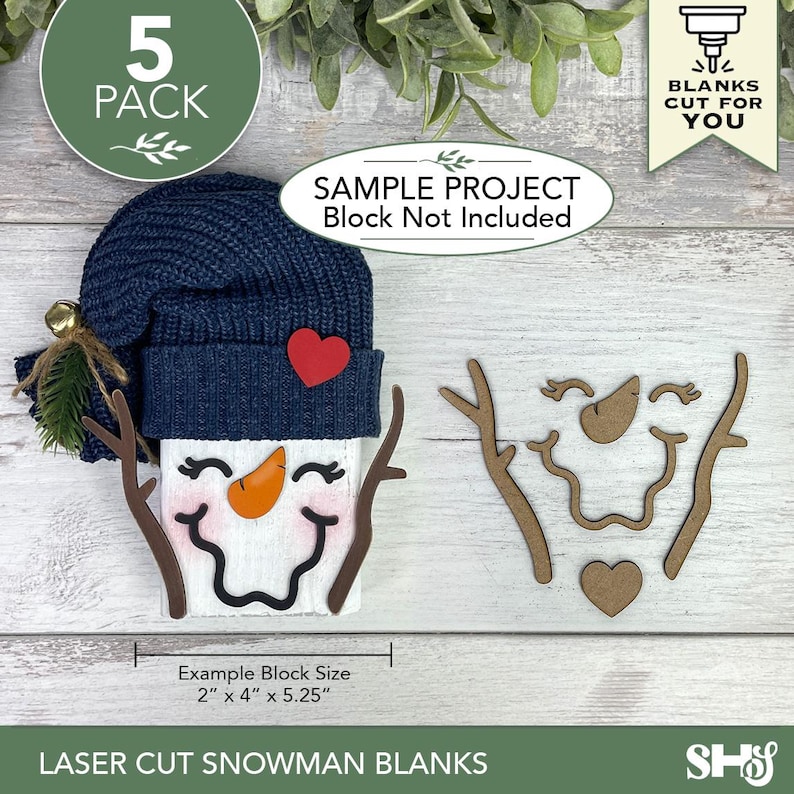 May include: A set of five laser-cut wooden snowman blanks including branch arms, a carrot nose, a mouth, and a heart. One assembled snowman features a navy blue knit hat, a red heart accent, and a painted face. Text includes 5 PACK, BLANKS CUT FOR YOU, SAMPLE PROJECT Block Not Included, and Example Block Size 2" x 4" x 5.25".