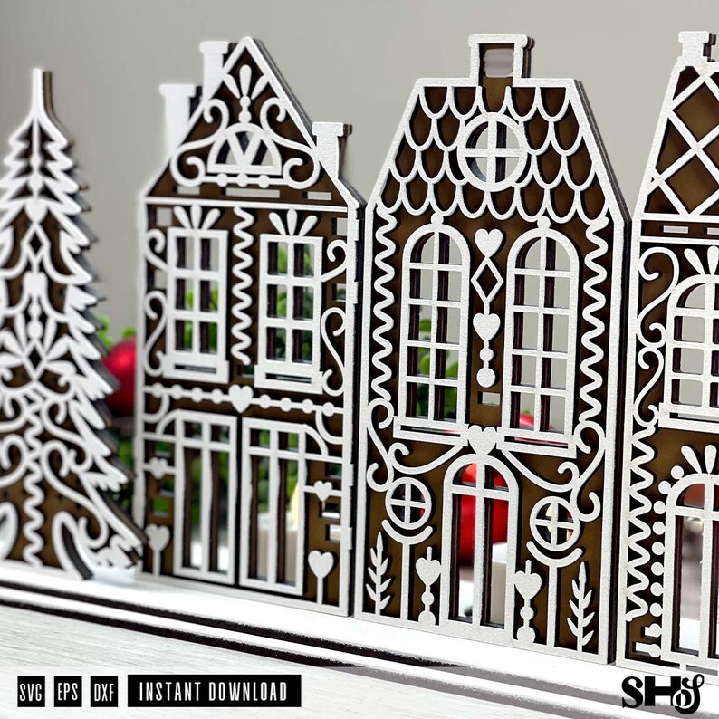 May include: A laser-cut wooden decorative set featuring a stylized evergreen tree and two intricate gingerbread-style houses with white filigree detailing on a dark brown base, designed as a digital file for instant download in SVG, EPS, and DXF formats.