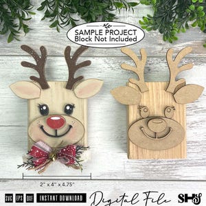 Pu&ograve; includere: Due decorazioni in legno a forma di renna, una dipinta con naso rosso e fiocco a motivi, l'altra in legno naturale. Ognuna presenta corna, orecchie e un volto su una base rettangolare. Testo: SAMPLE PROJECT Block Not Included, 5,08 cm x 10,16 cm x 12,07 cm.