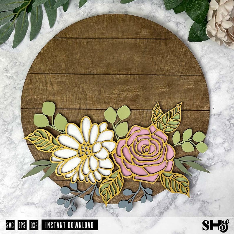 Op de afbeelding: Een rond houten bord met een bloemmotief. Het ontwerp bevat een roze roos, een witte madeliefje en groene bladeren. Het bord is perfect voor een boerderij- of rustieke inrichting.