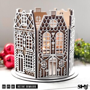 May include: A brown and white laser-cut gingerbread house lantern featuring intricate architectural details, arched windows, heart-shaped accents, and a scalloped roof design. The structure is circular, crafted from layered panels with cutouts.