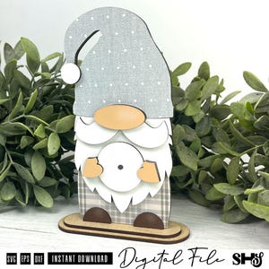 May include: A layered gnome cutout featuring a grey hat with white polka dots, a tan nose, a white beard, and a plaid patterned body. The gnome stands on a two-tiered base and includes the text SVG, EPS, DXF, INSTANT DOWNLOAD, Digital File, SHS.