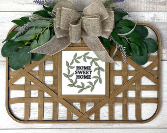 May include: A wooden sign with a woven frame and a burlap bow. The sign says "Home Sweet Home" in black text with a green leaf wreath around it.