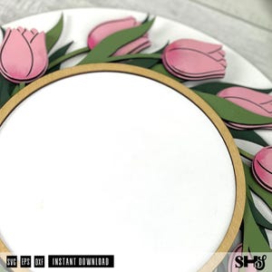 May include: A circular wooden sign featuring a white center panel framed by a light wood border. The outer edge is decorated with layered pink tulip flowers and dark green leaves. The text SVG, EPS, DXF, INSTANT DOWNLOAD, and SHS is visible.