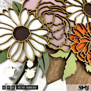 May include: A wooden floral bouquet with a white daisy, a pink rose, and an orange flower. The flowers are outlined in gold and have a layered, dimensional look.