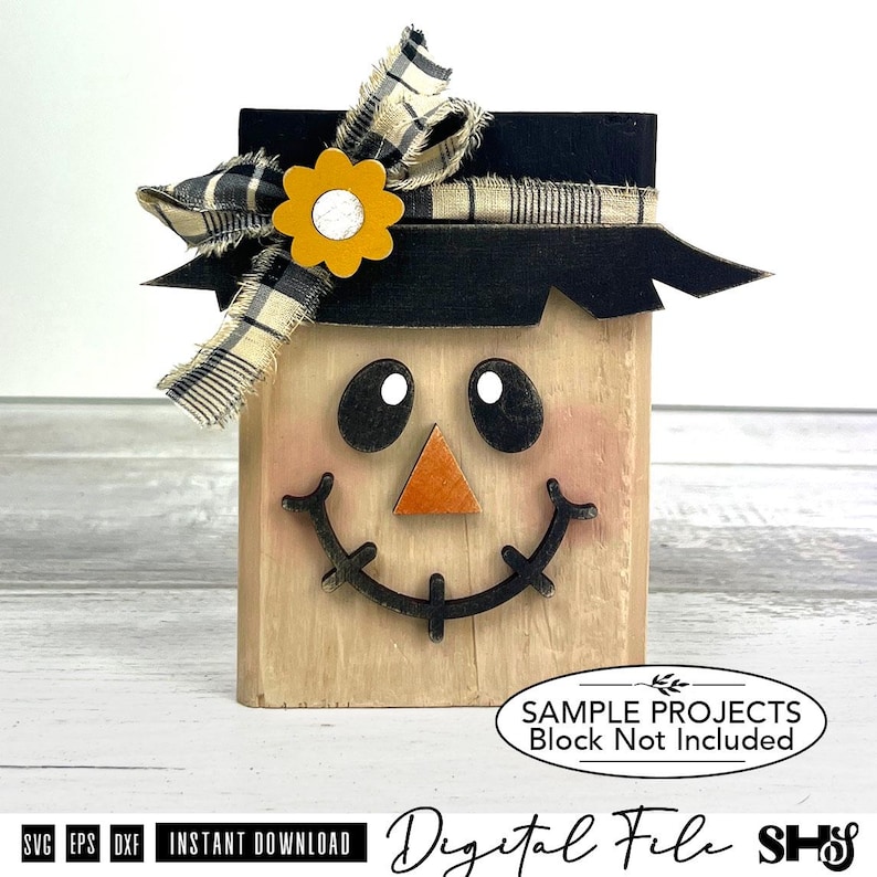 May include: A rectangular wooden block decoration featuring a painted scarecrow face with black oval eyes, a triangular orange nose, and a stitched black smile. A black brimmed hat sits on top, adorned with a plaid fabric bow and a yellow flower.