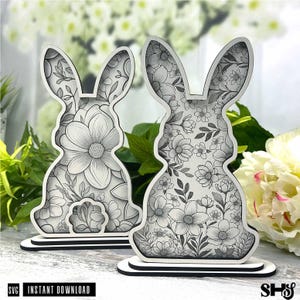 May include: Two wooden cutout bunny shapes with a floral design. The bunnies are standing on a white base. The design is black and white.