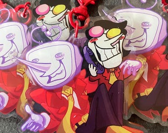 May include: Acrylic keychains featuring a cartoon character with a white face, black hair, and yellow and pink glasses. The character is wearing a red suit and purple pants. The keychains have red heart-shaped clasps.