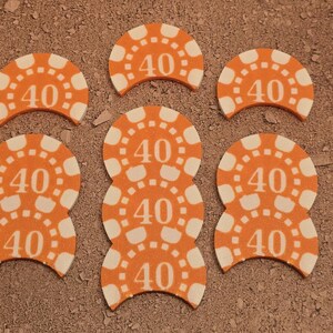 May include: Six orange and white plastic chips with the number "40" printed on them. The chips are shaped like half circles and are arranged in a semi-circle pattern.